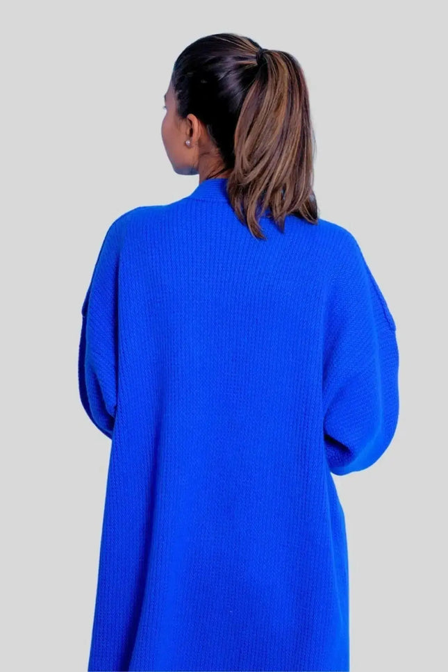a woman in a blue sweater standing in front of a wall 